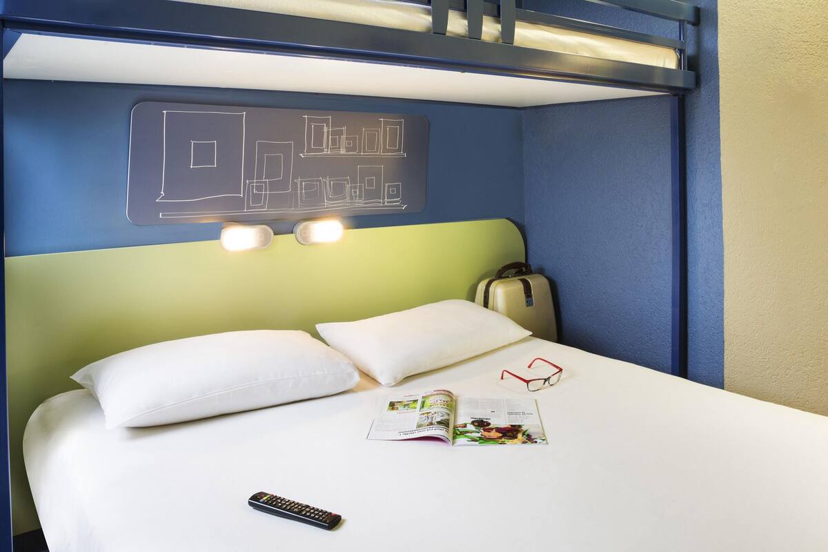 A bunk bed with a headboard, a suitcase, a remote control, and a magazine on the bed.