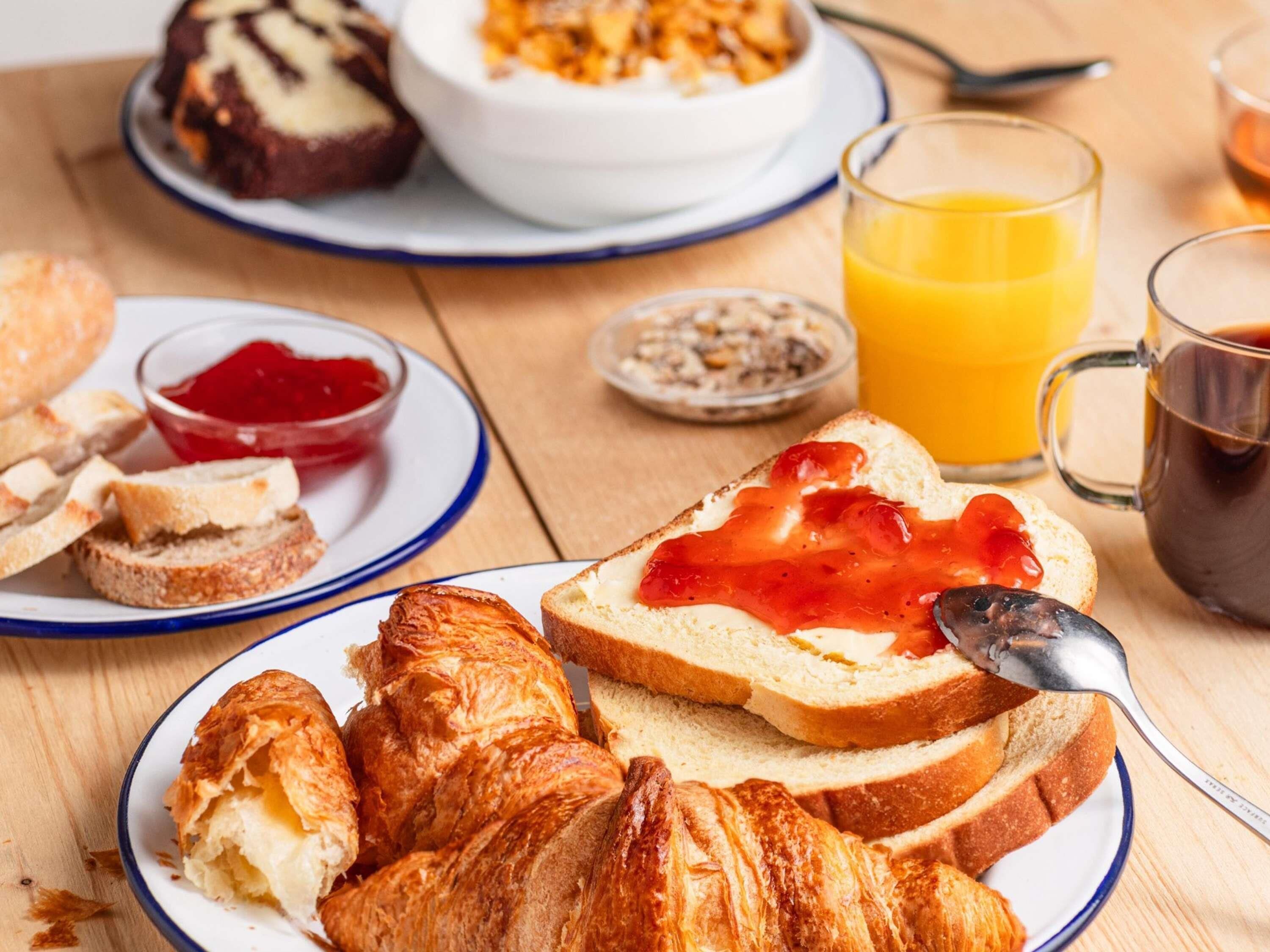 A breakfast setting with bread, croissants, jam, and a glass of orange juice.