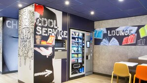 A lounge area with a vending machine, a coffee machine, and a table with chairs. - ibis budget Thonon Les Bains (Thonon-les-Bains)