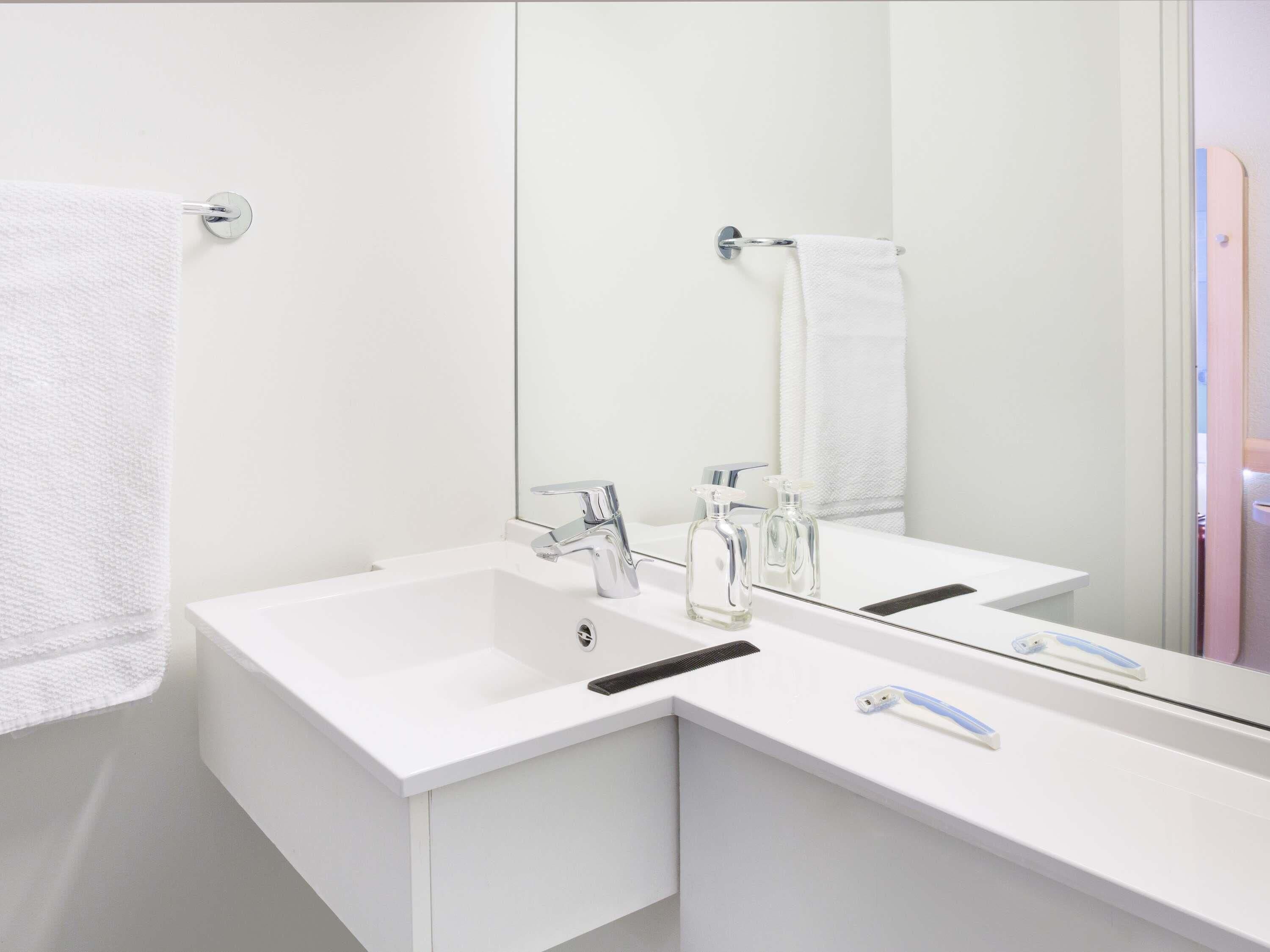 A modern bathroom with two sinks, a large mirror, and a towel rack.