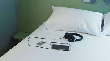 A bed with white pillows, a green headboard, and a pair of headphones on the bed.
