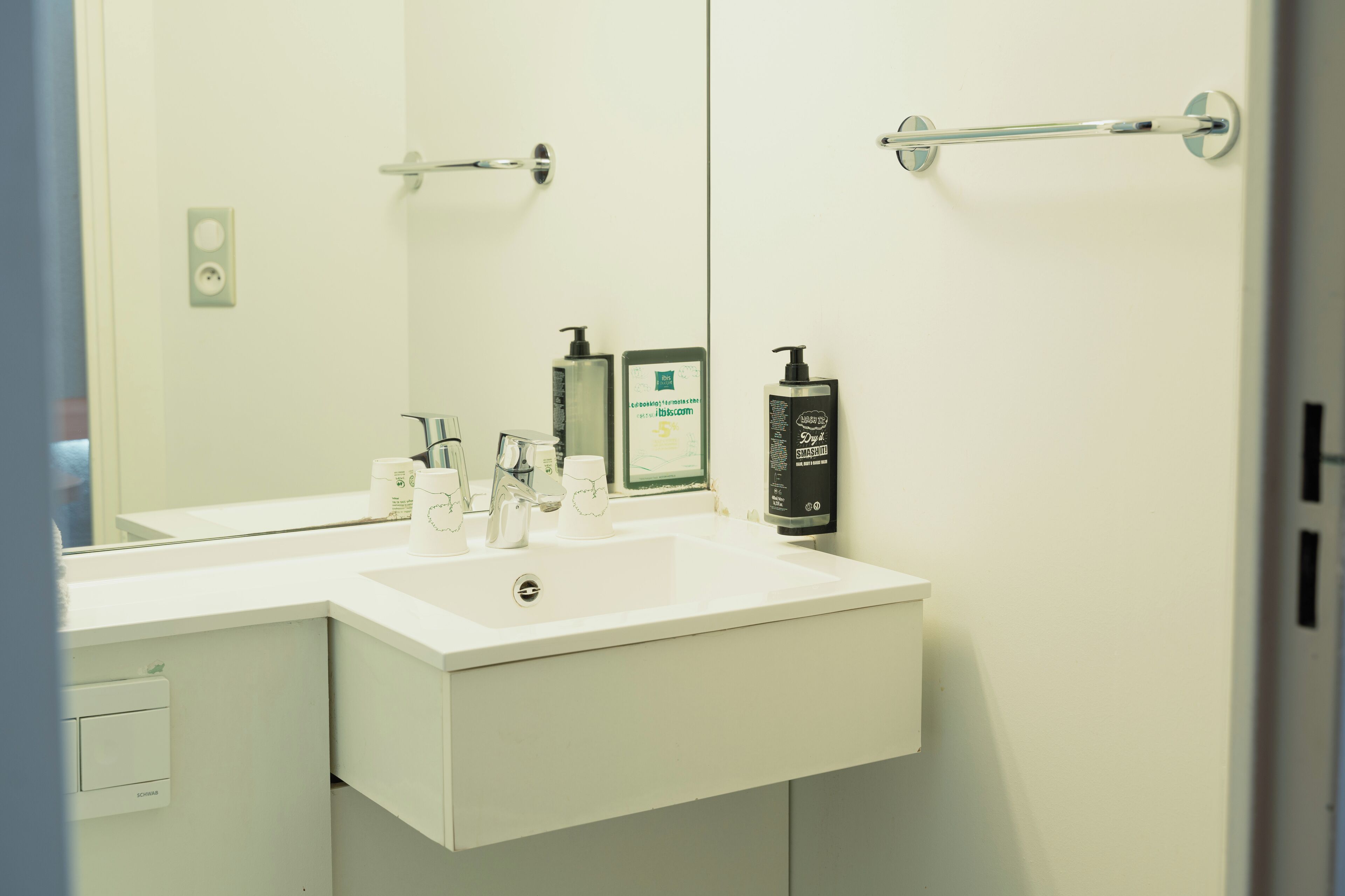 A modern bathroom with a white sink, a large mirror, and a towel rack.