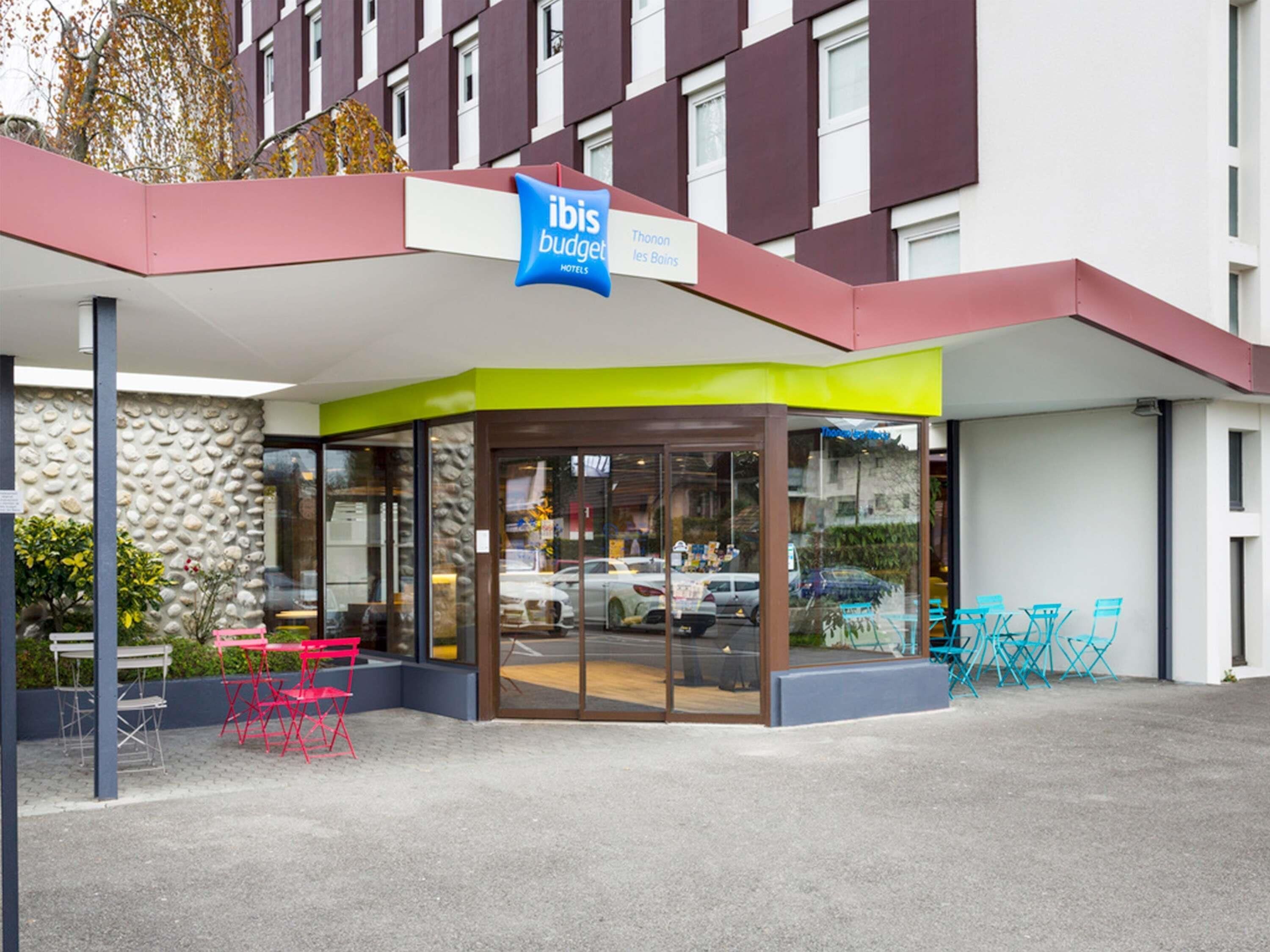 A hotel entrance with a glass door, a sign for ibis budget hotels, and outdoor seating.