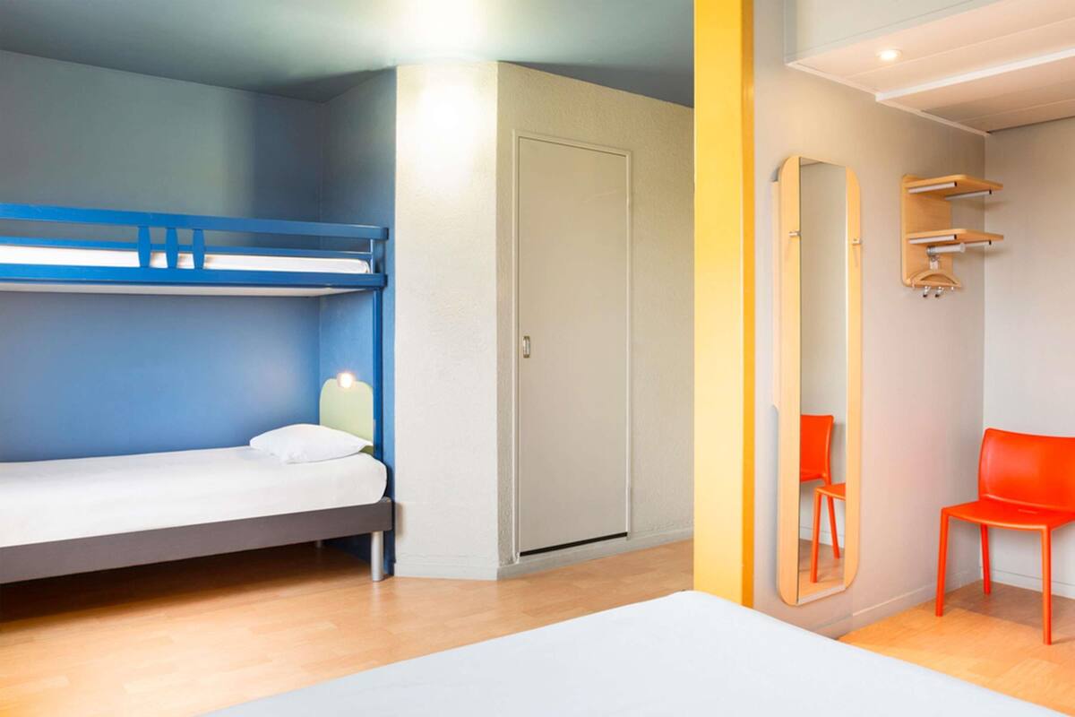 A room with a bunk bed, a single bed, a door, a mirror, and a red chair.
