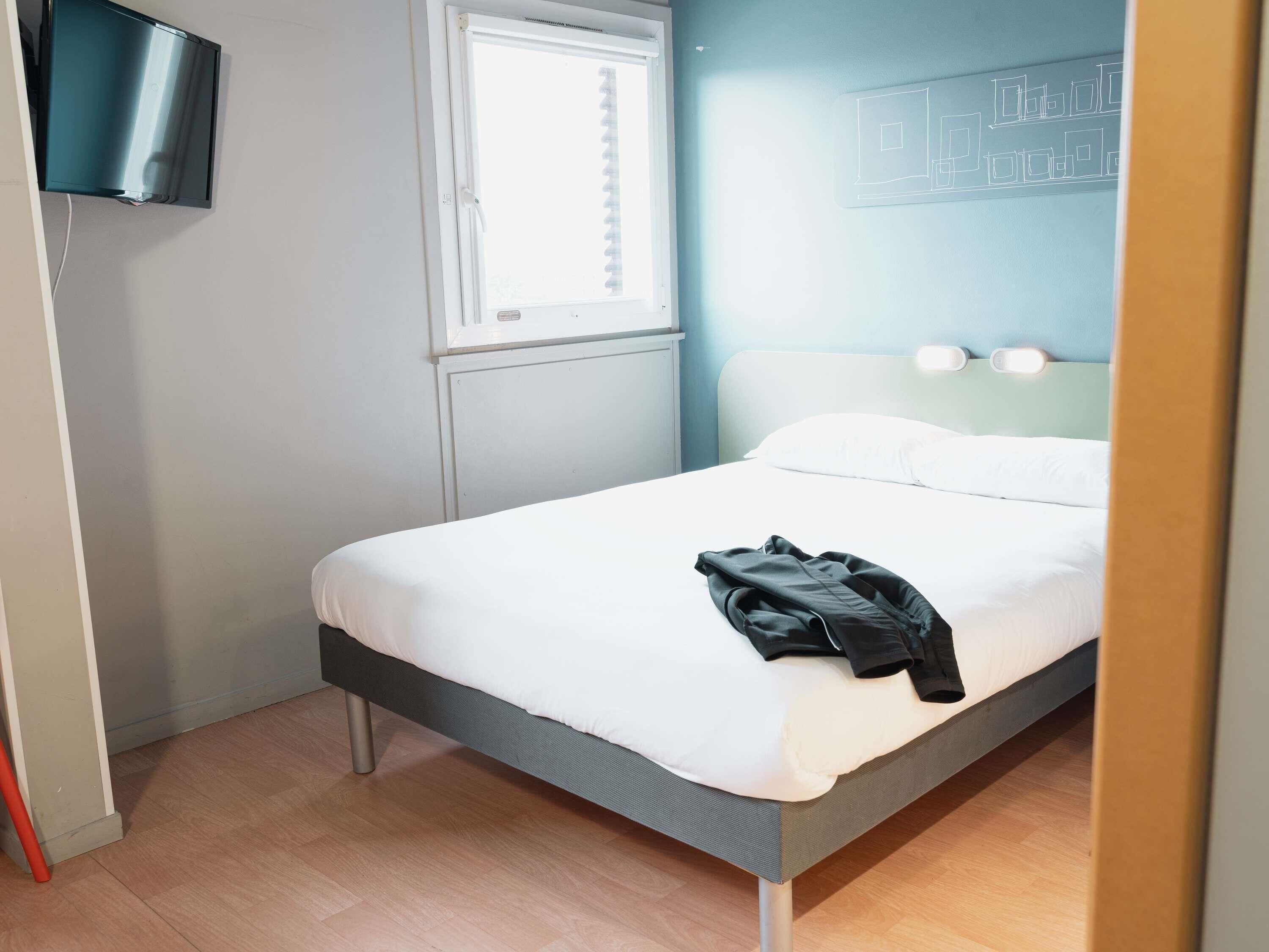 A bedroom with a bed, a television mounted on the wall, and a window.