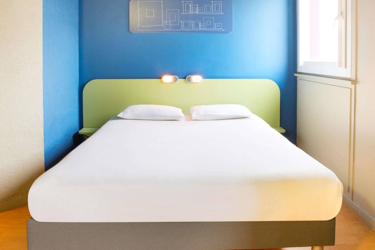 A bed with a green headboard, white bedding, and a wall-mounted light fixture.