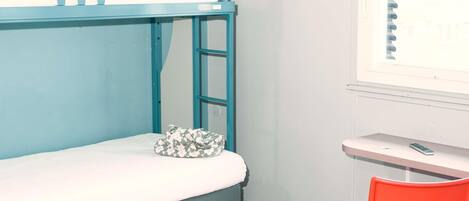 A bunk bed with a mattress and a pillow, a desk with a chair, and a window with blinds.