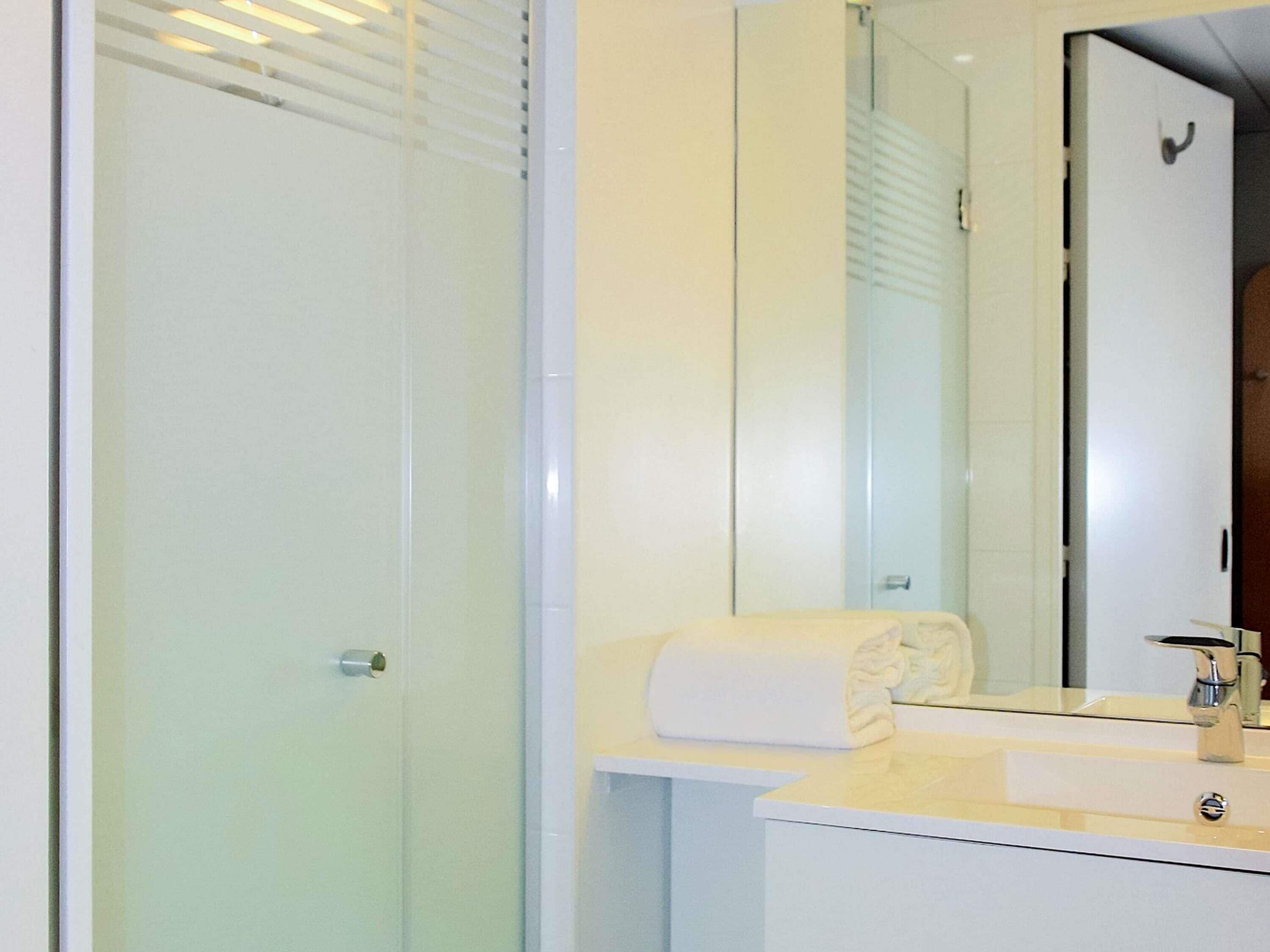 Une salle de bain moderne avec une douche à parois de verre, un lavabo blanc avec un miroir et une serviette posée sur le comptoir.