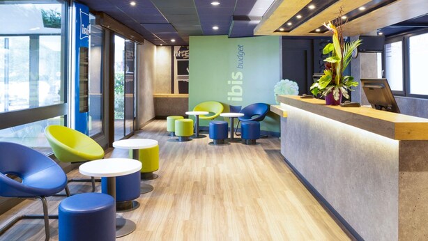 A modern interior with a reception desk, colorful chairs, and a green wall with 'ibis budget' text. - ibis budget Thonon Les Bains (Thonon-les-Bains)
