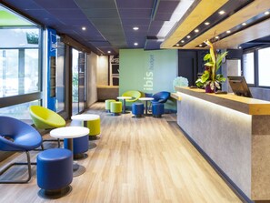A modern interior with a reception desk, colorful chairs, and a green wall with 'ibis budget' text. - ibis budget Thonon Les Bains (Thonon-les-Bains)