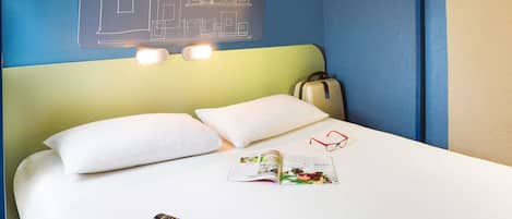 A hotel room with a bunk bed, a bedside table with a remote control, a magazine, and a suitcase.