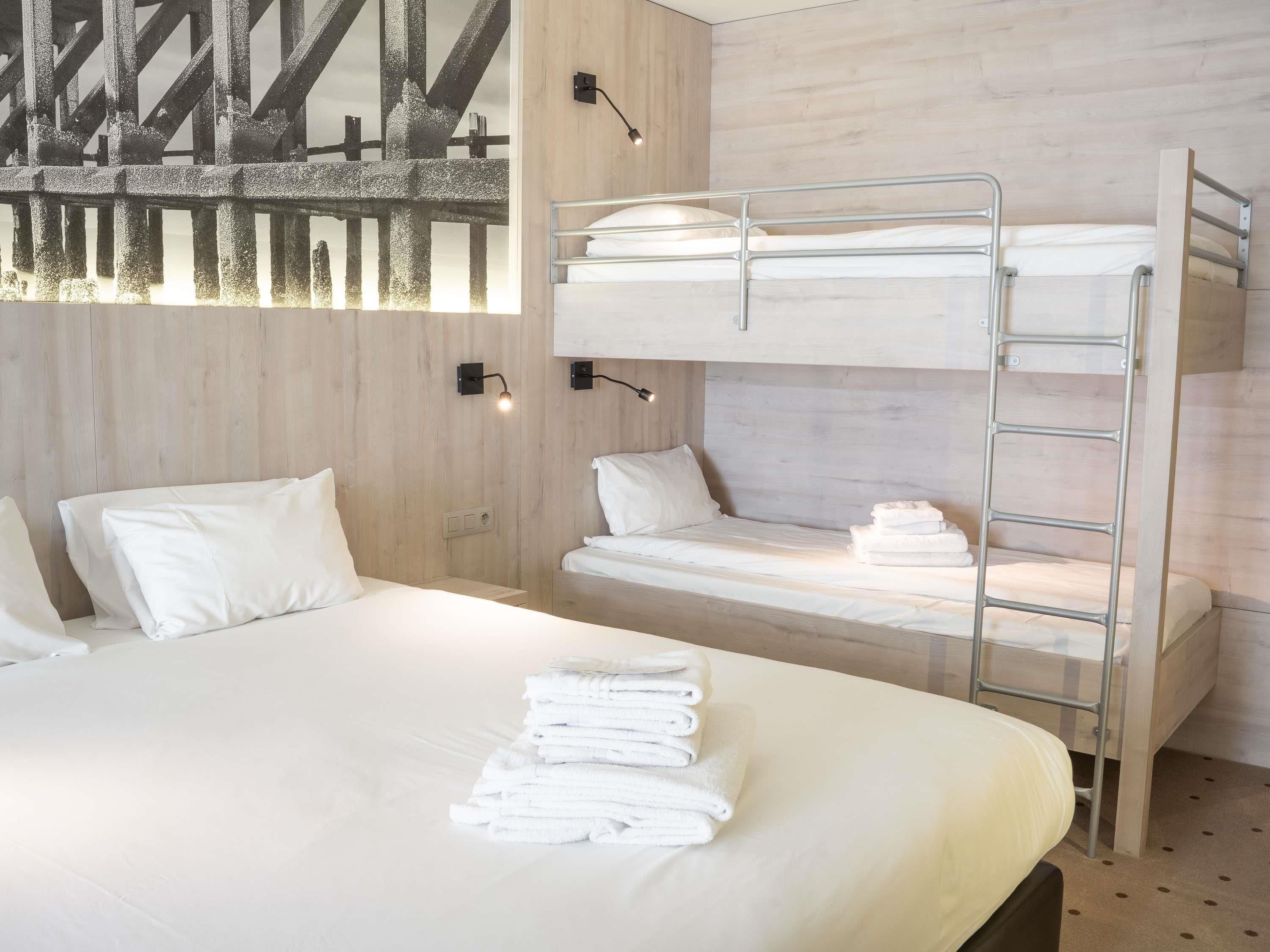 A bunk bed with a ladder, a single bed with pillows, and a wall-mounted light fixture.