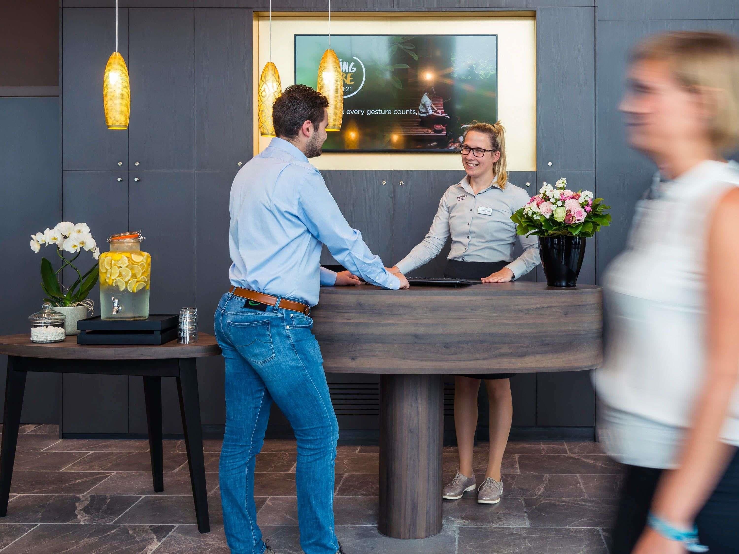 A reception desk with a modern design, a digital screen displaying a message, and a vase with flowers.