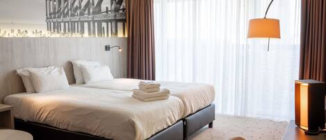 Una habitación de hotel con una cama, un escritorio, una silla, una lámpara y un ventanal con cortinas.