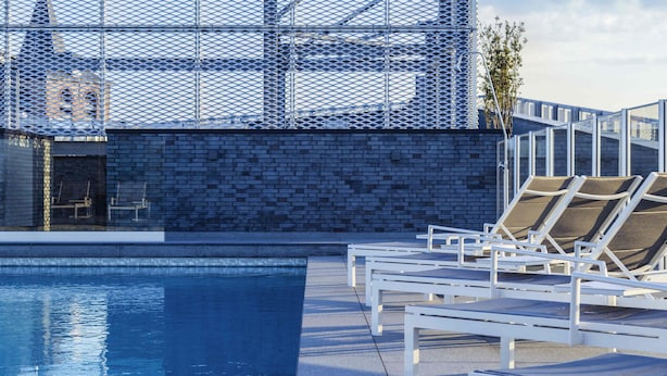 A poolside area with lounge chairs and a view of a building with a distinctive lattice facade.