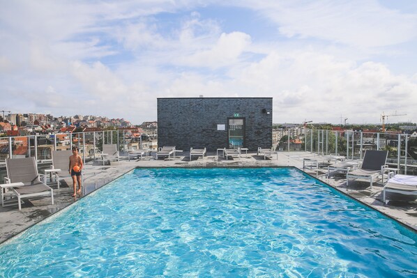 Ein Pool auf dem Dach mit Liegestühlen und einem kleinen Gebäude im Hintergrund.