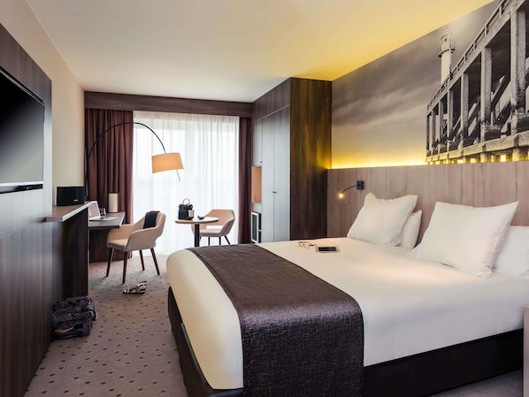 Une chambre d’hôtel avec un lit, un bureau, des chaises et une grande fenêtre avec des rideaux.
