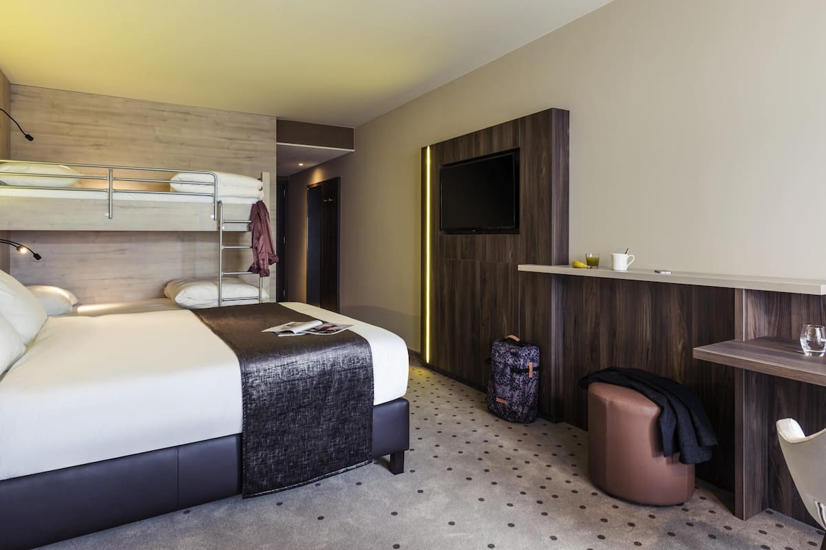 Habitació d'hotel moderna amb llit superposat, escriptori, televisió i una petita zona de seients.