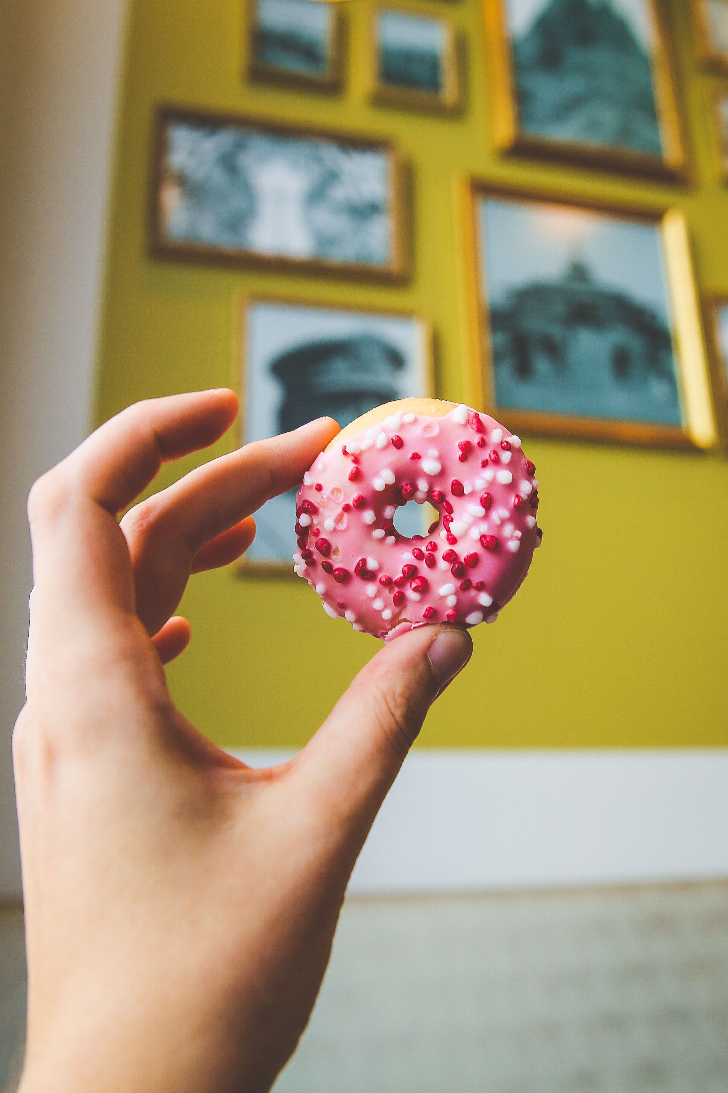 A hand holding a pink frosted donut with white sprinkles.