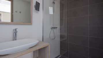 Une salle de bain moderne avec un grand lavabo blanc, un miroir et une douche séparée par des parois en verre.