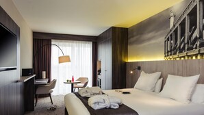 A hotel room with a bed, desk, chair, and a large window with curtains.