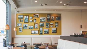 A restaurant interior with tables, chairs, a counter, and a wall decorated with framed pictures.