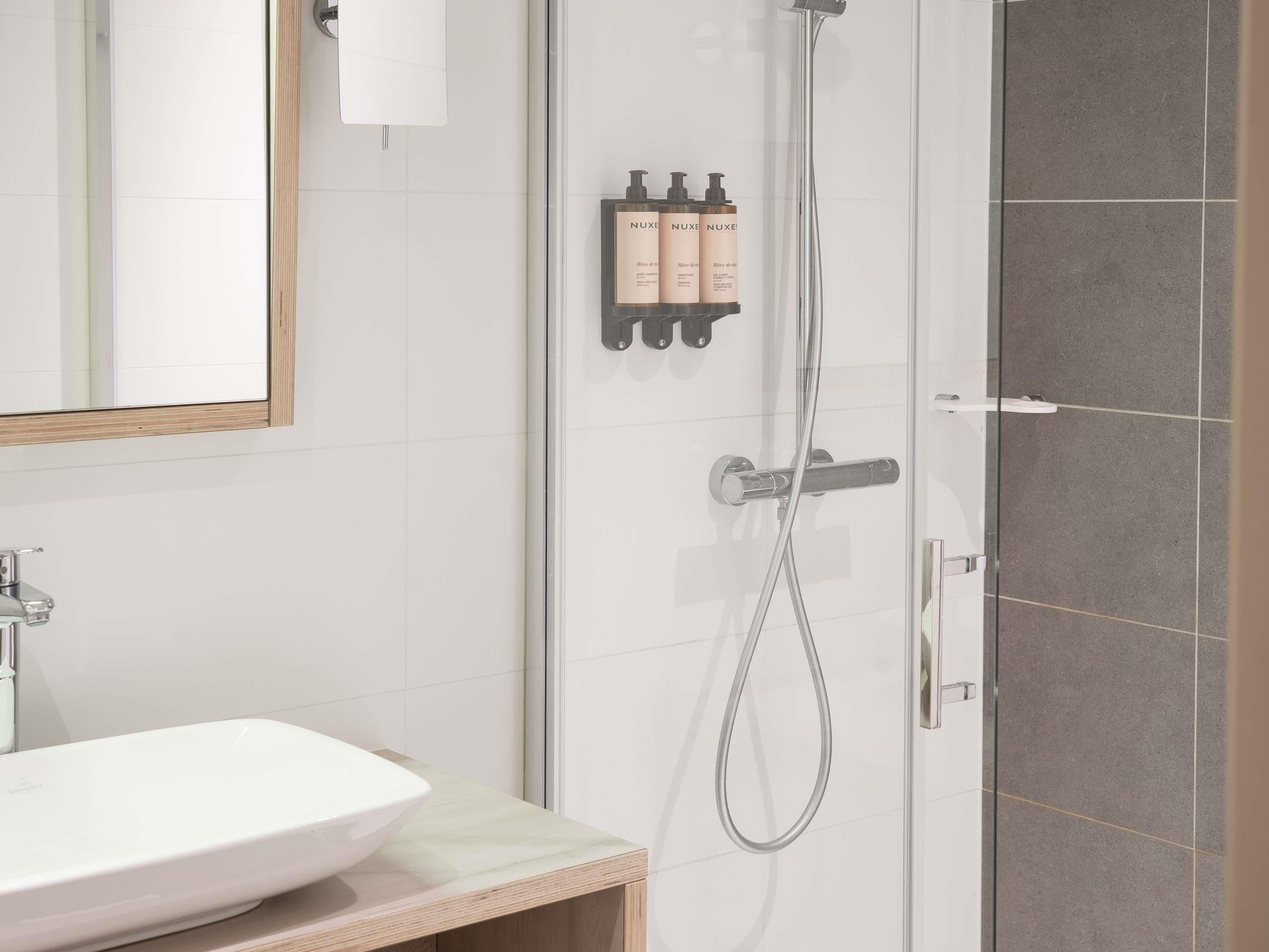 Une salle de bain moderne avec une douche à parois de verre, un lavabo blanc et un miroir.