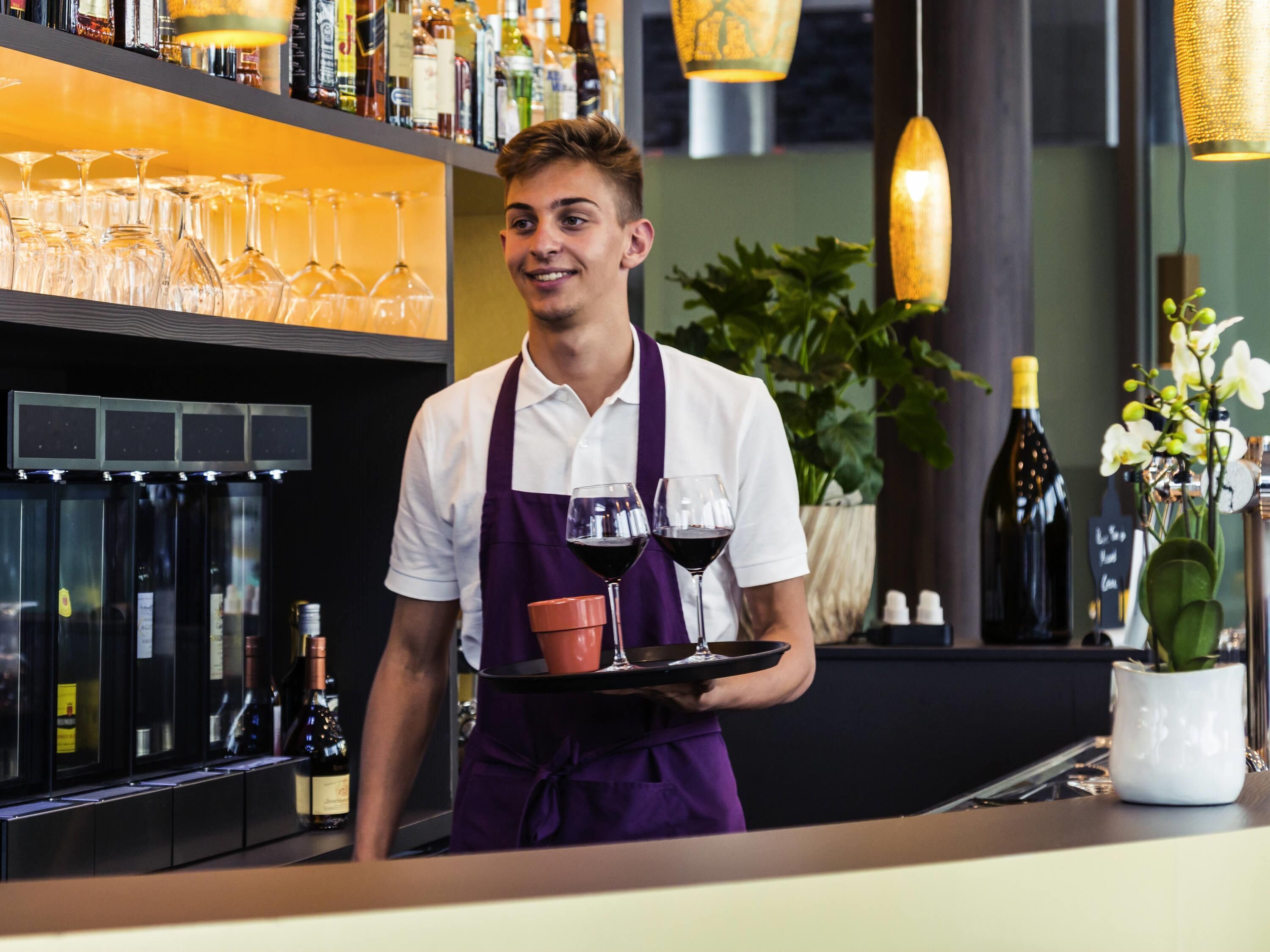 A bar area with a bartender holding a tray with glasses and bottles.