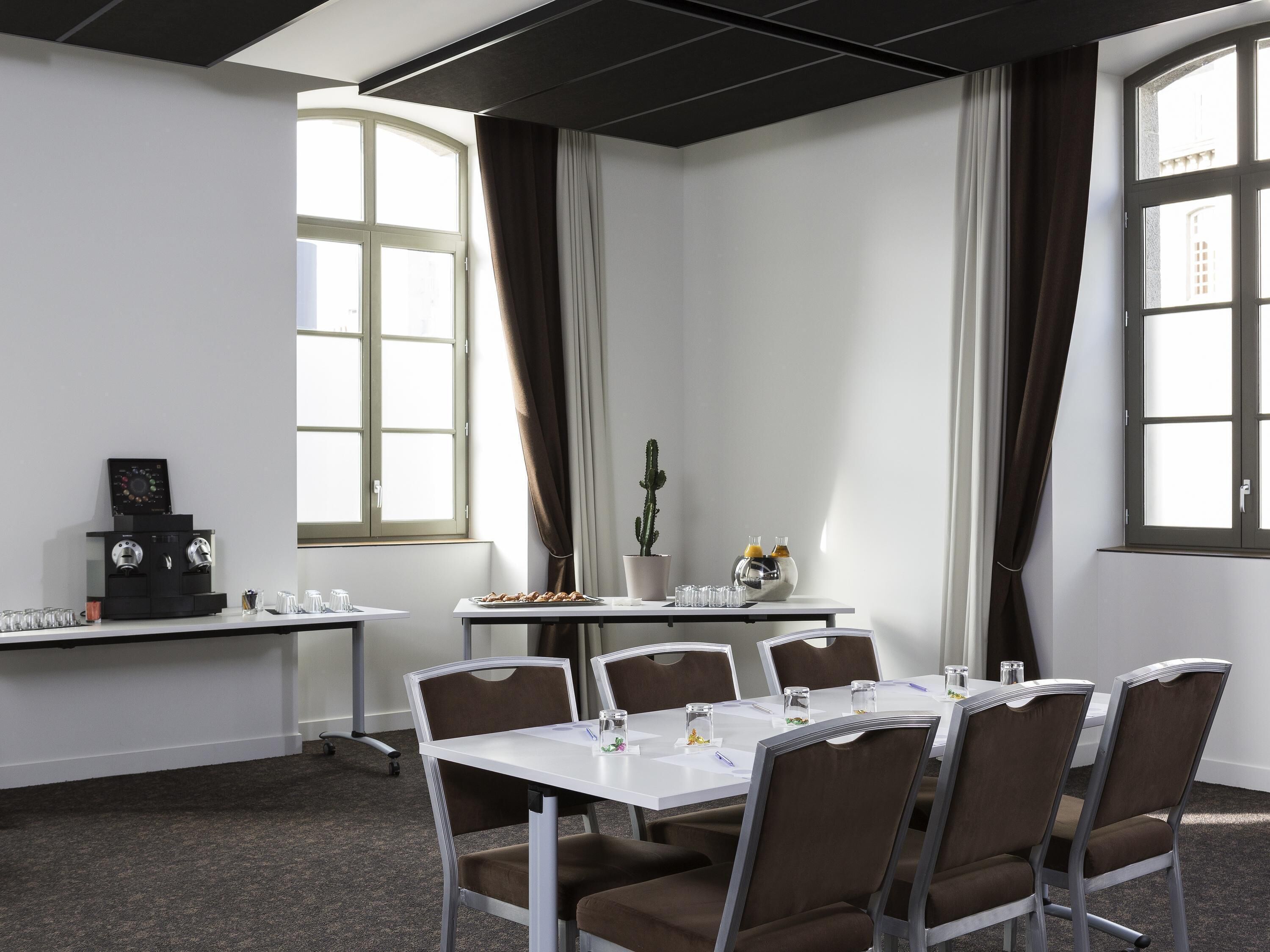 Una sala de conferències amb taula blanca, cadires marrons, una màquina de cafè i una planta de cactus.