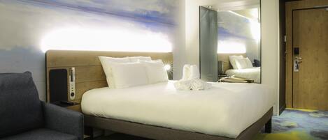 A modern hotel room with a large bed, a seating area with a chair, a wooden door, and a large mirror.