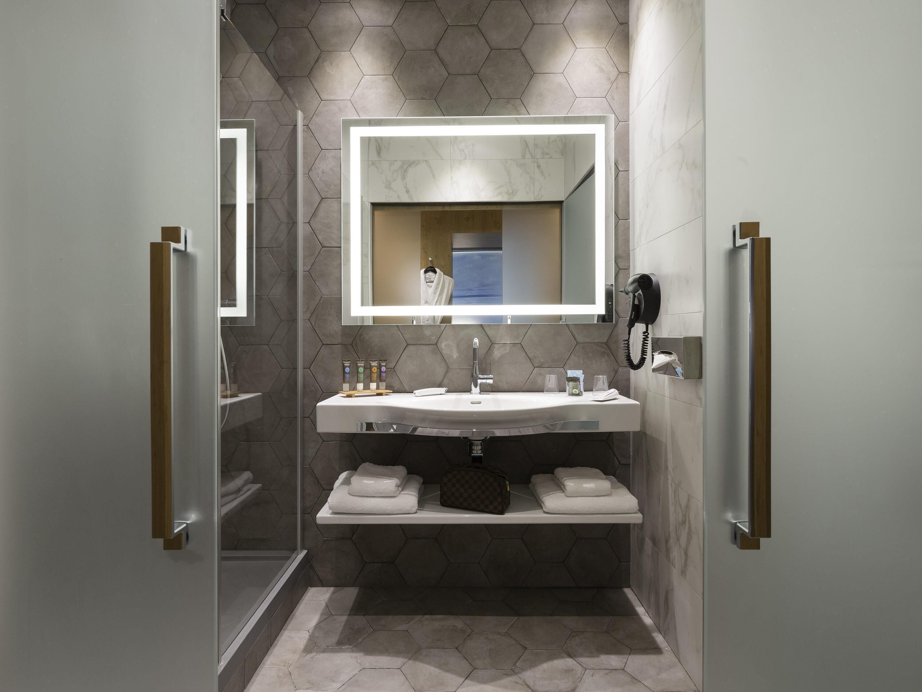 Un baño moderno con un espejo grande, un lavamanos, un perchero para toallas y una ducha.