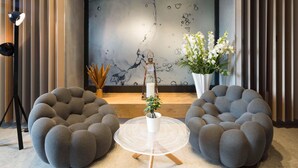 Una sala de estar moderna con dos sillones orejeros grises y texturizados, una mesa redonda blanca y una planta en maceta.