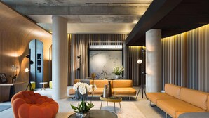 Un área de descanso moderna con una mesa de centro redonda, un sillón de saco naranja y sofás beige.