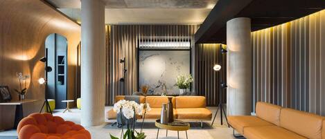 Un área de descanso moderna con una mesa de centro redonda, un sillón de saco naranja y sofás beige.