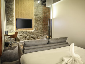 Habitación de hotel con pared de piedra, panel de madera, televisor de pantalla plana, escritorio con silla y cama con toalla blanca.