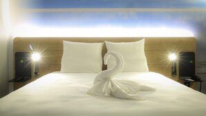 Habitación de hotel con cama, dos almohadas, una toalla con forma de cisne, lámparas de noche y mesita de noche con teléfono.