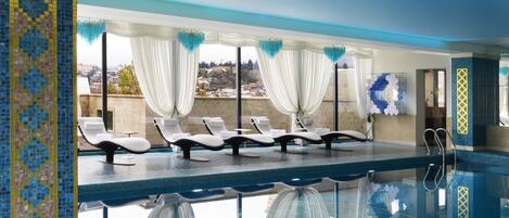 Zona de piscina con sillones de descanso y vistas de la ciudad.
