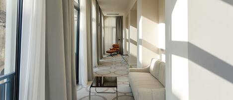 A corridor with a sofa, a chair, and a table, leading to a window with curtains.