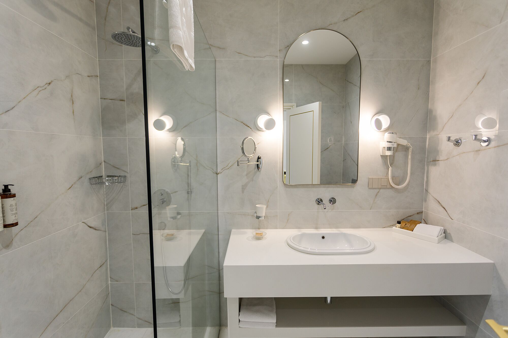 Un baño moderno con ducha envuelta en vidrio, un lavamanos blanco y un espejo grande.