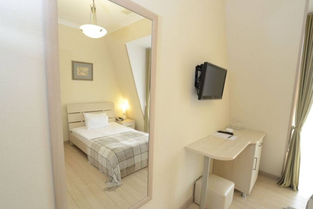 Habitació d'hotel amb llit, taula de nit, làmpada, escriptori, cadira i televisió penjada a la paret.