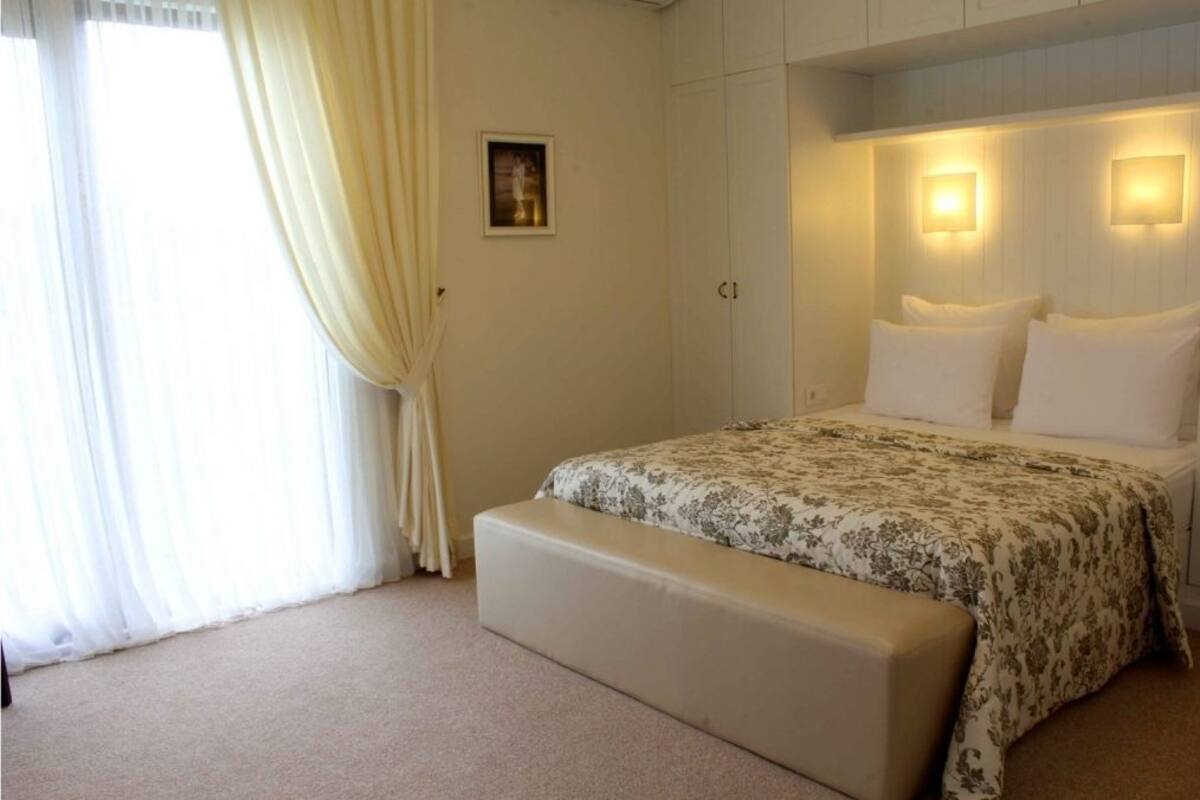 Un dormitori amb llit, una banca, una finestra amb cortines i llums penjades a la paret.