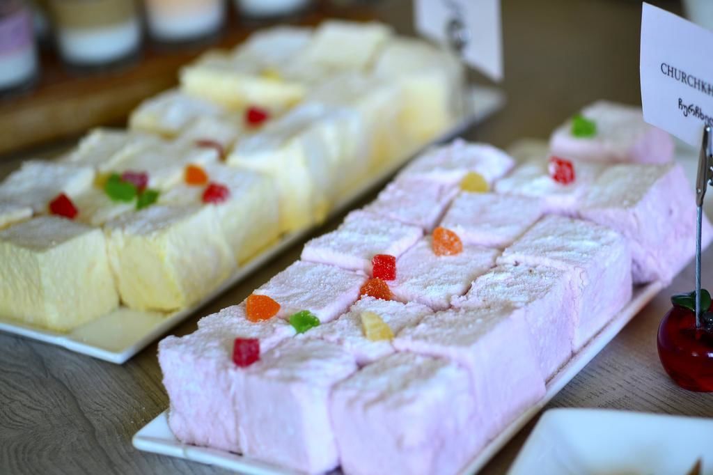 Exposição de sobremesas com diversos tipos de bolo e doces, incluindo um bolo rosado com cobertura e balas coloridas.