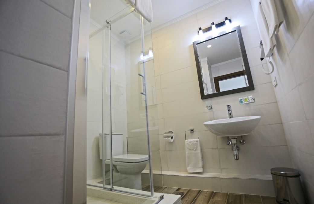 Un baño moderno con cabina de ducha de vidrio, un lavamanos blanco y un espejo sobre él.