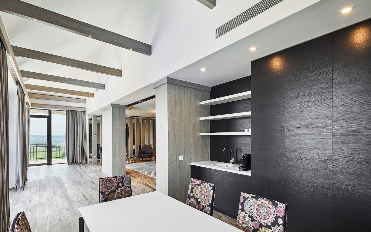 Une chambre d’hôtel moderne dotée d’un grand balcon, d’un coin repas avec une table blanche et de lambris en bois foncé.