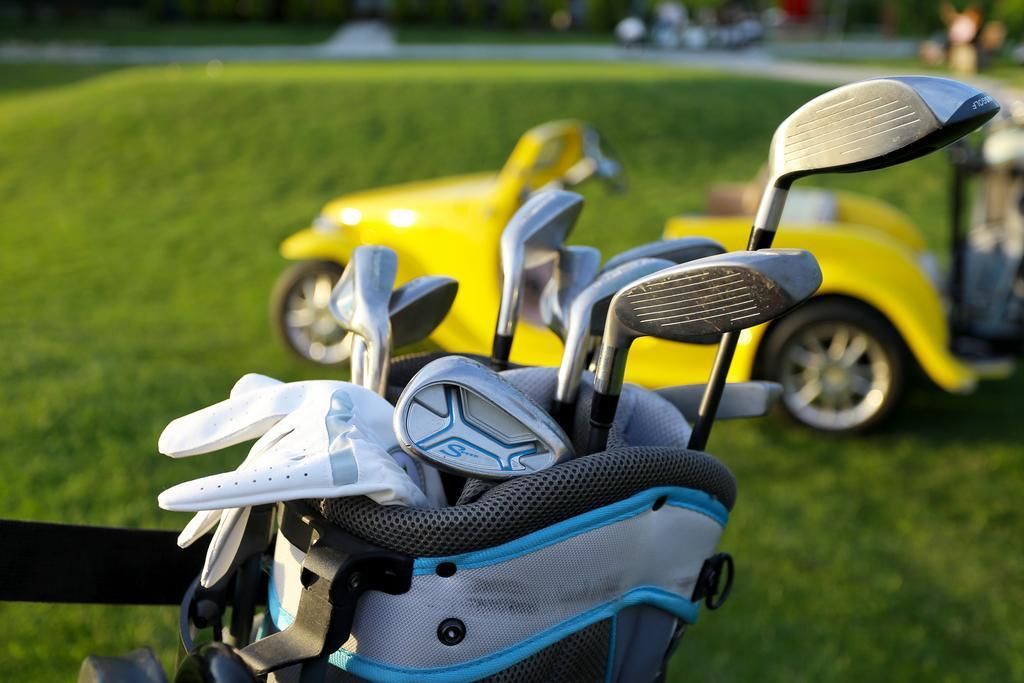 A golf bag with multiple clubs and a yellow golf cart in the background.