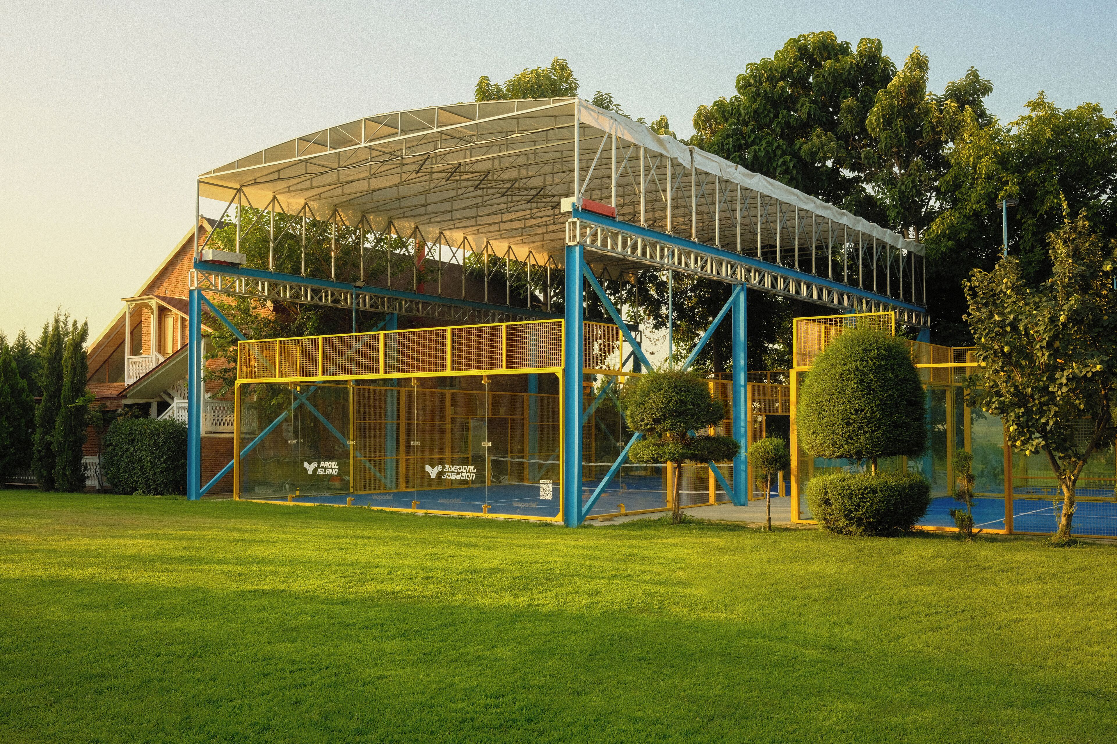 Un edificio moderno con fachada de vidrio, elementos estructurales azules y un área exterior cubierta.