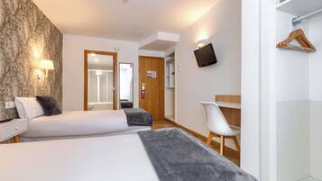 A hotel room with two beds, a desk, a chair, a TV, and a wardrobe.