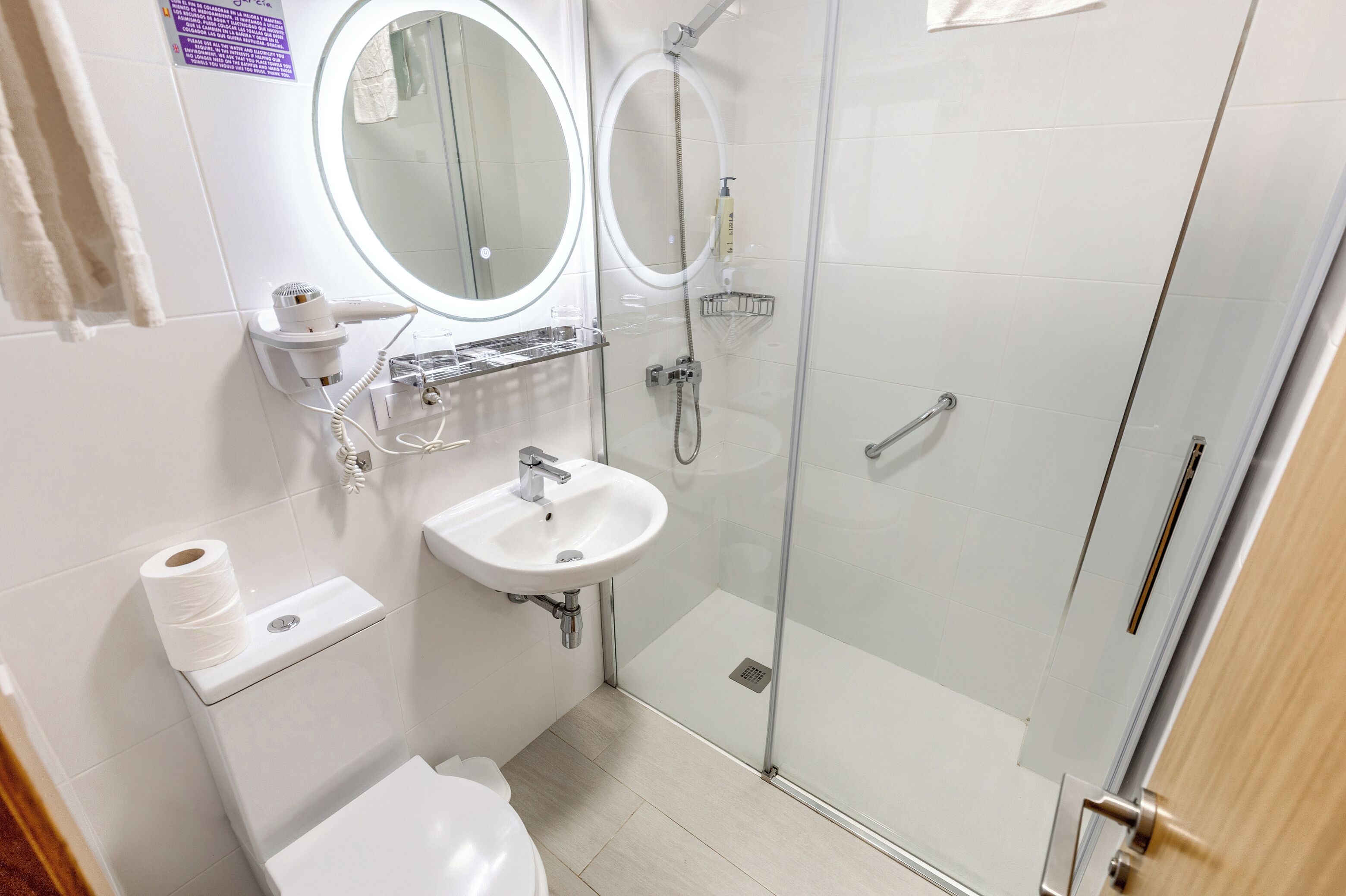 Un baño moderno con inodoro, lavamanos, espejo y ducha con mampara de vidrio.
