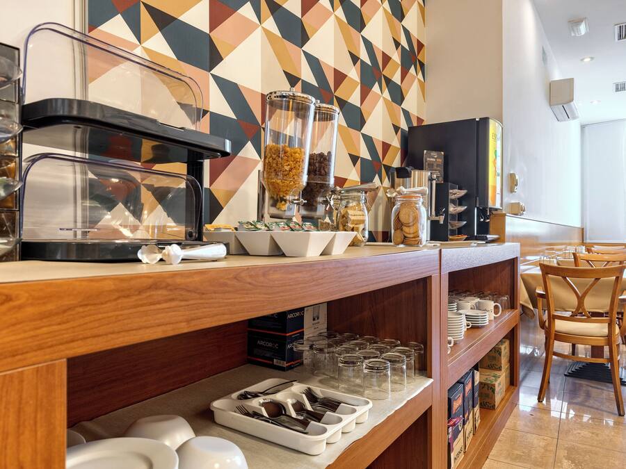 Een ontbijtbuffet met een koffiezetapparaat, cornflakes en potjes met toevoegingen.
