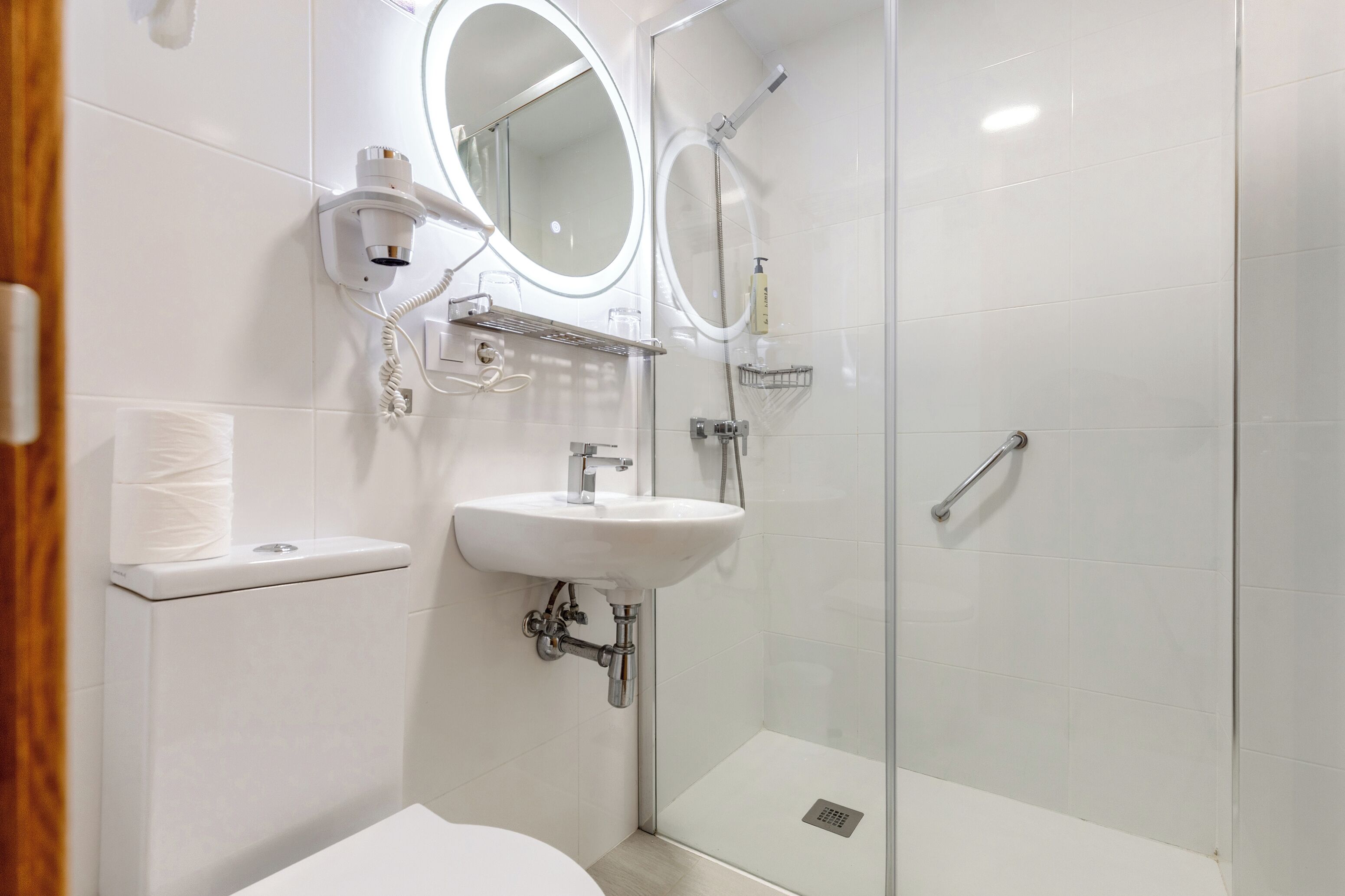 Un baño moderno con cabina de ducha de vidrio, un lavamanos blanco con espejo y un inodoro con dispensador de toallas de papel.